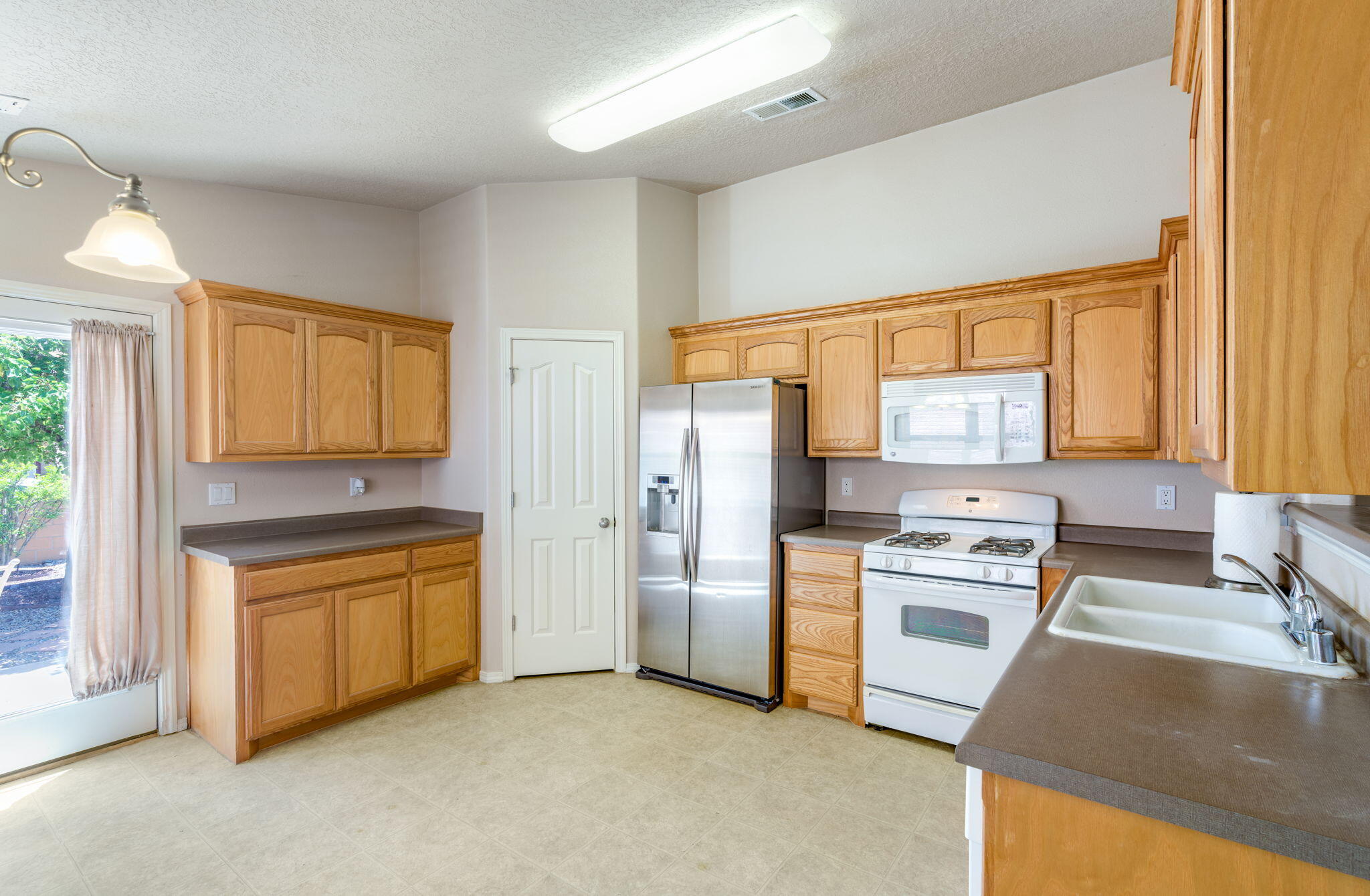 Eat-in kitchen at 806 Vargas Drive with warm wood cabinetry, gray counters, pantry, refrigerator, range, microwave, sink, and patio-door access.