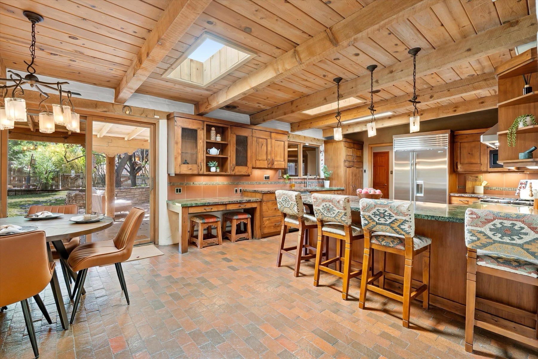 Large Los Ranchos kitchen with wood cabinetry, exposed beams, skylights, stainless appliances, brick flooring, and counter seating.