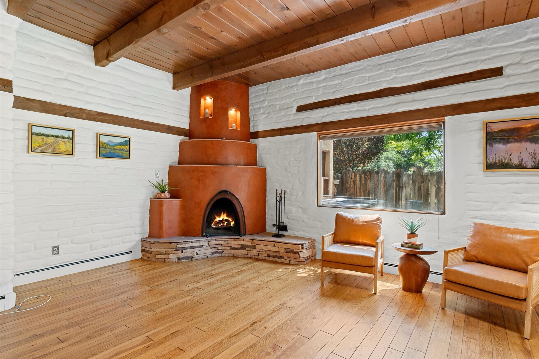 Living room with wood-beamed ceiling, wood flooring, white-painted adobe walls, and a sculptural fireplace at 4068 Dietz Farm Circle NW.