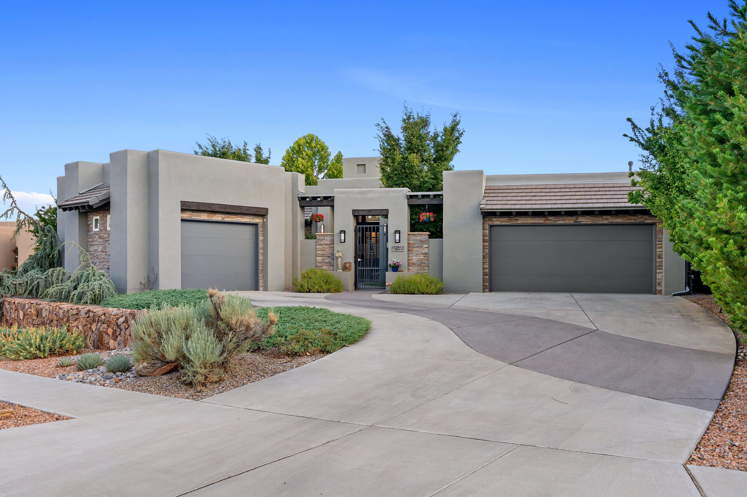 Exterior of 4908 Camino Valle Trail NW in Albuquerque, showing a Southwest Contemporary home with stone accents, gated courtyard entry, xeriscape landscaping, and three-car garage configuration.