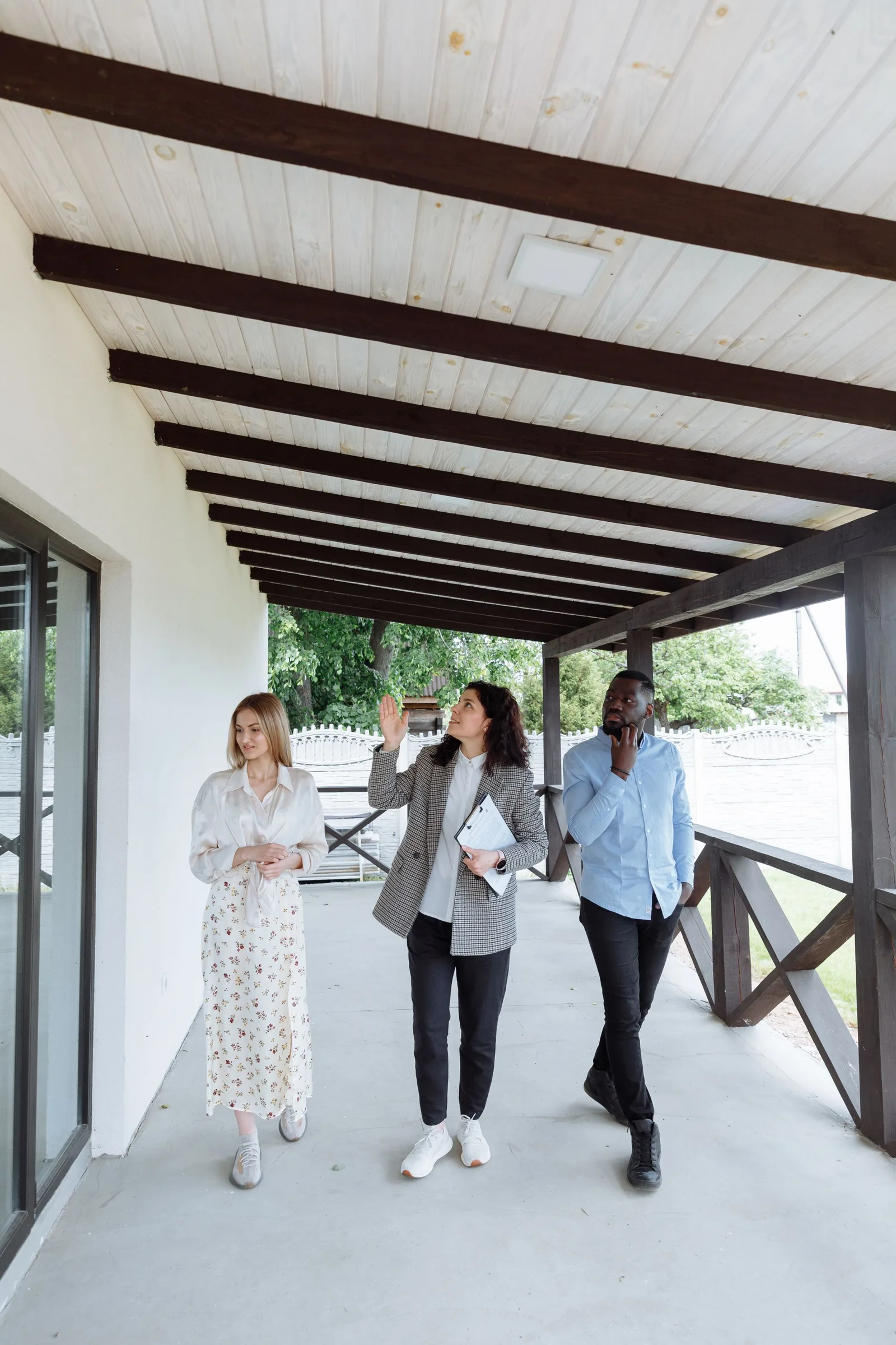 A real estate professional discussing a home's exterior with two prospective buyers.