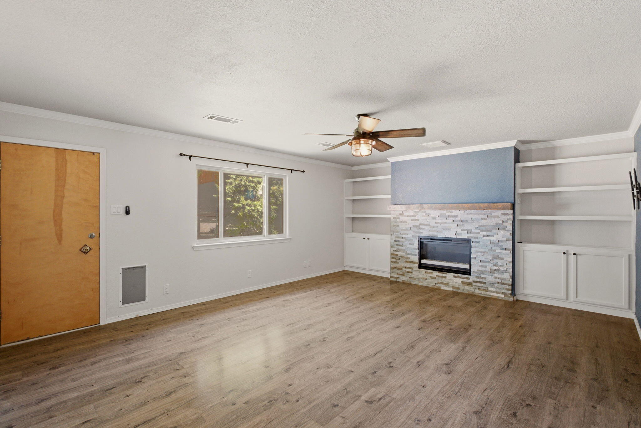 Main living room with wood-look flooring, built-in shelving, and a stacked-stone fireplace
