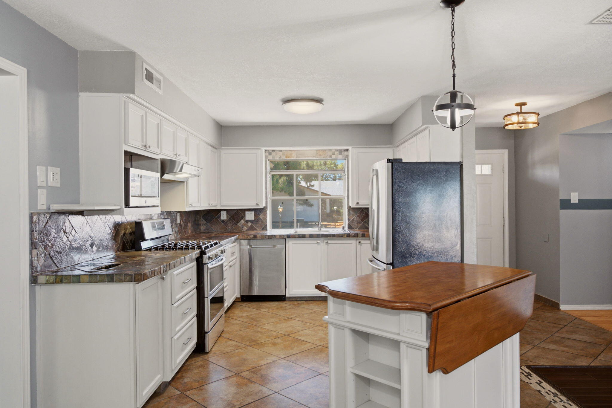 Updated kitchen with white cabinetry, stainless appliances, tiled counters, and a compact island