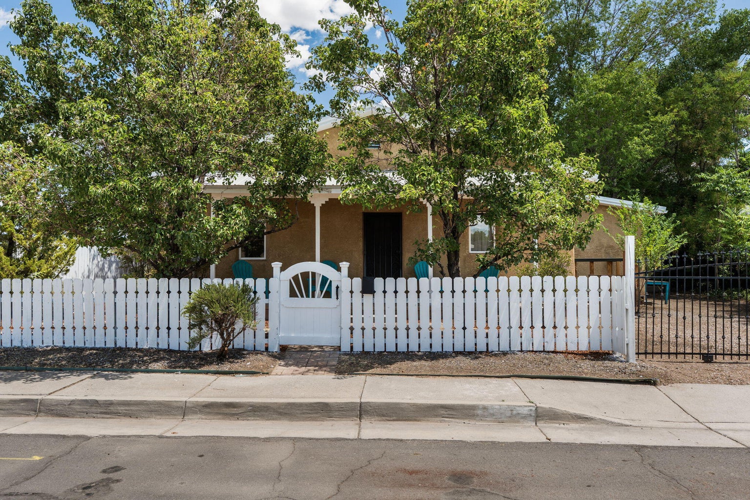 Front exterior of 1023 11th Street SW in Albuquerque, with a covered porch, mature trees, and a gated front yard
