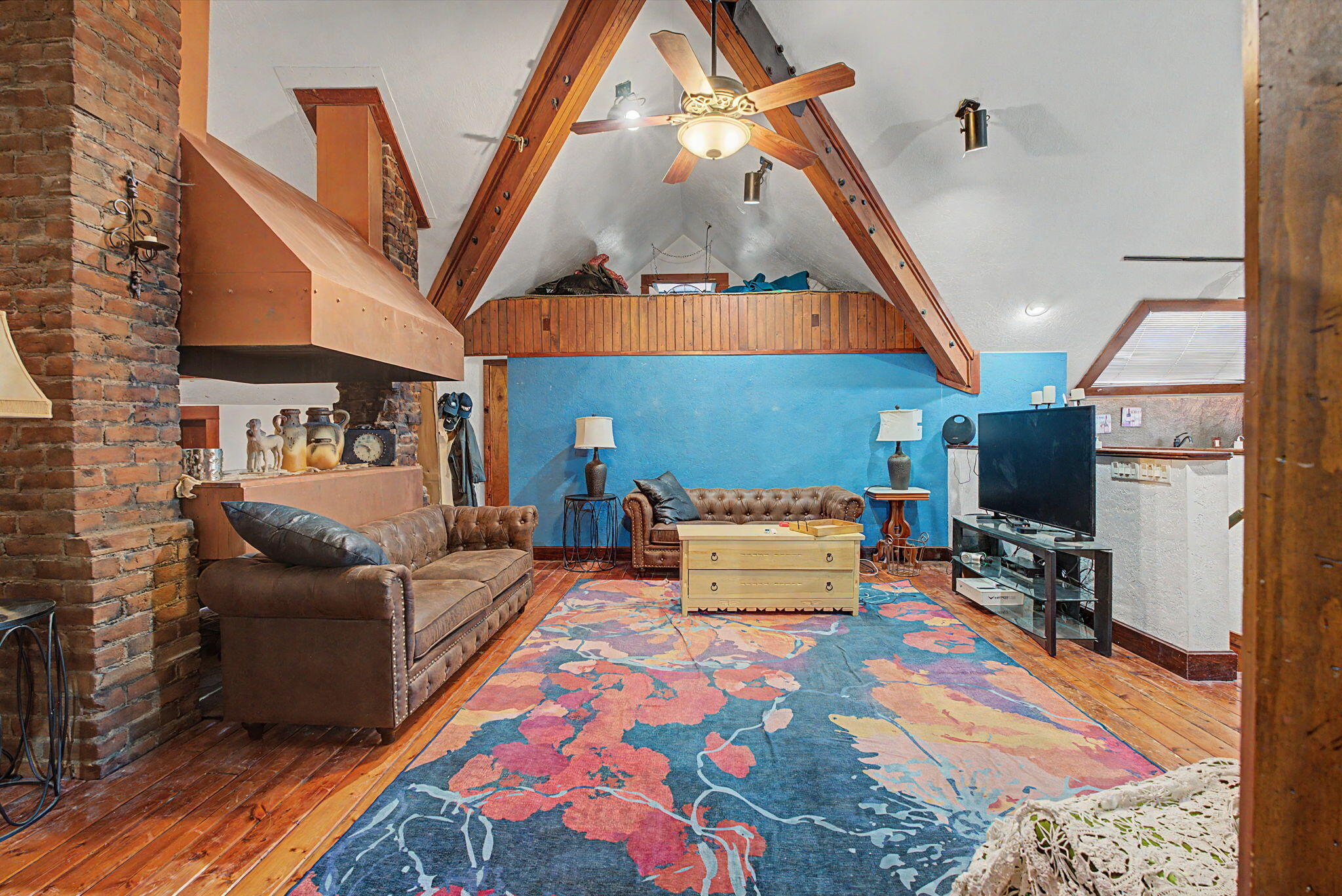 Vaulted great room with exposed beams, wood floors, and a brick chimney