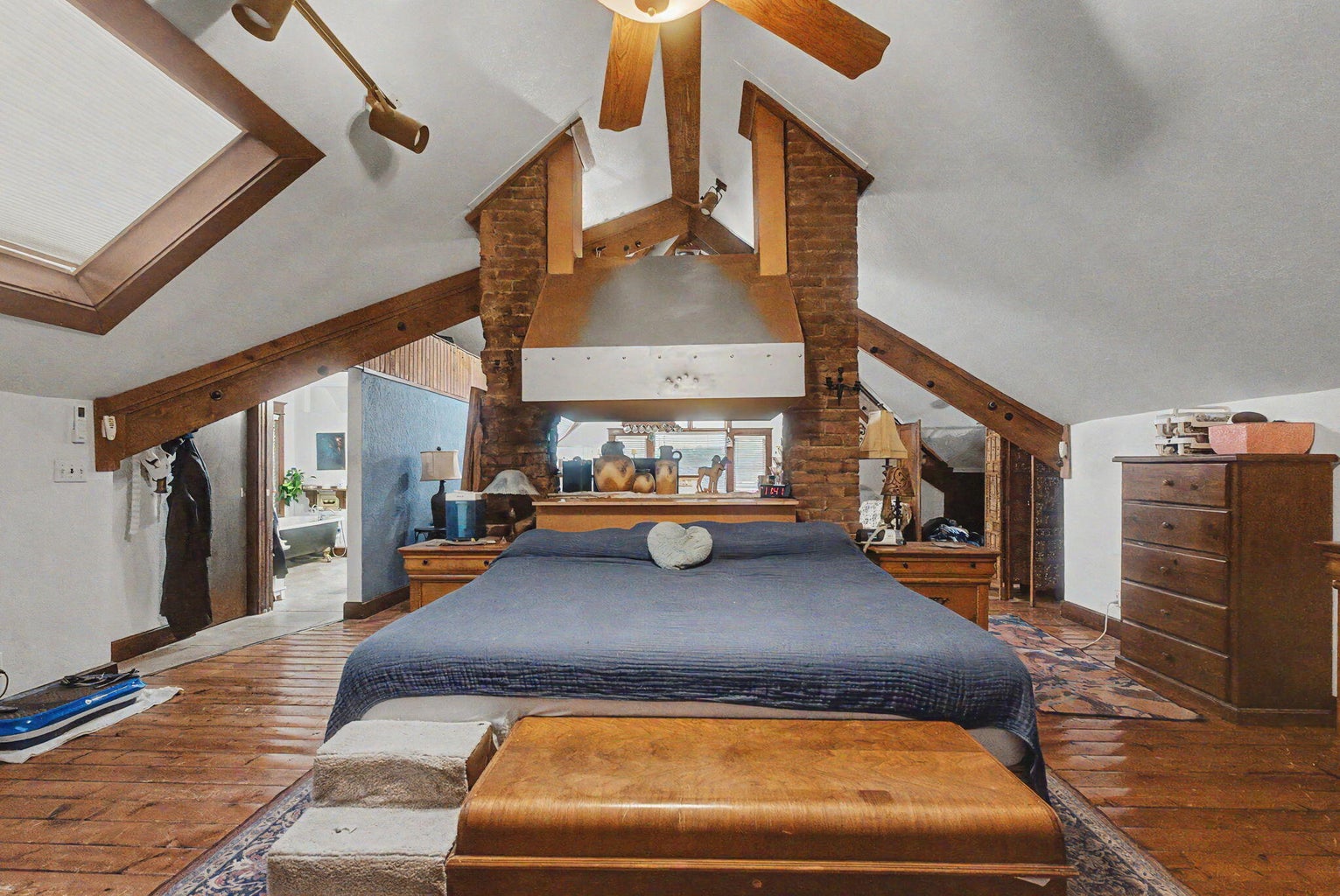 Upstairs bedroom suite with exposed beams, brickwork, wood floors, and angled ceilings