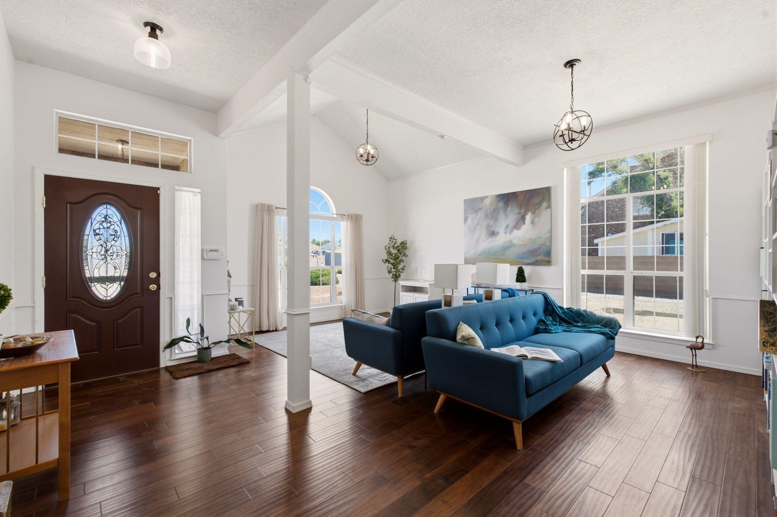 Bright front living area at 1684 Savannah Court NE in Rio Rancho, with tall arched windows, wood flooring, and a blue sofa.