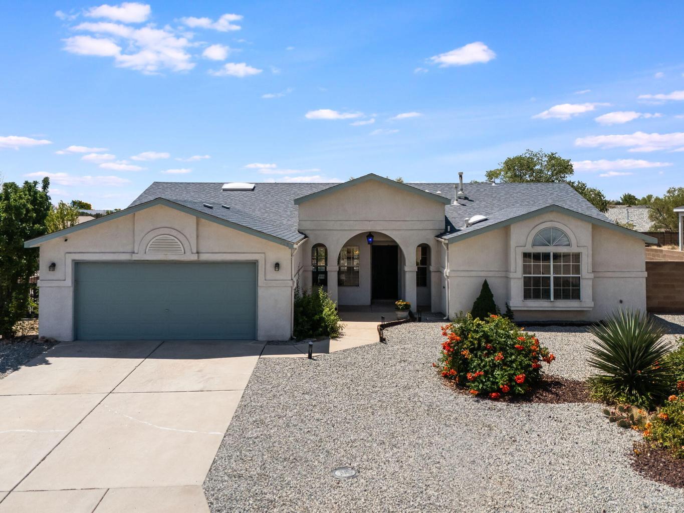 Front exterior of 7250 Pelona Court NE in Rio Rancho with a two-car garage, arched entry, stucco finish, and xeriscaped front yard