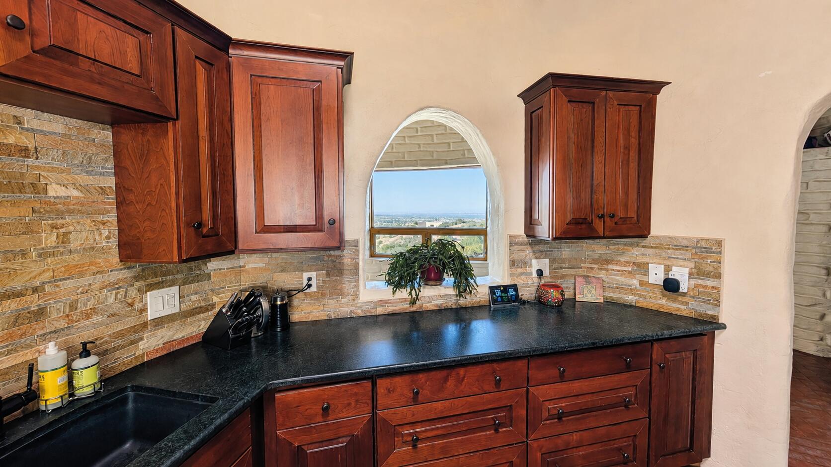 Kitchen with soapstone counters, warm wood cabinetry, and an arched window framing the Albuquerque view