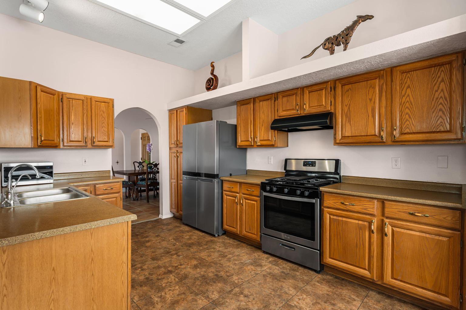 Kitchen at 7250 Pelona Court NE with wood cabinetry, peninsula sink, gas range, skylight, and an arched opening toward the breakfast area