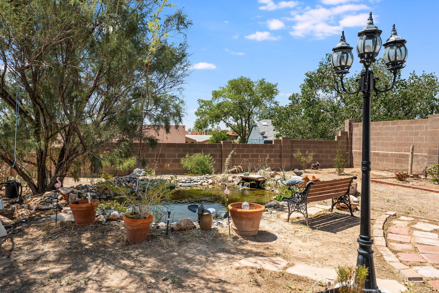 Koi pond and water feature in the backyard at 7250 Pelona Court NE with a bench, mature trees, and a walled yard