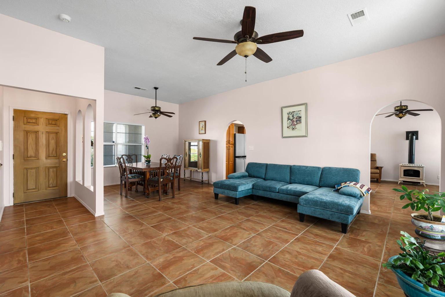 Main living and dining area at 7250 Pelona Court NE showing tile floors, arched openings, ceiling fans, and a pellet stove in the adjoining room