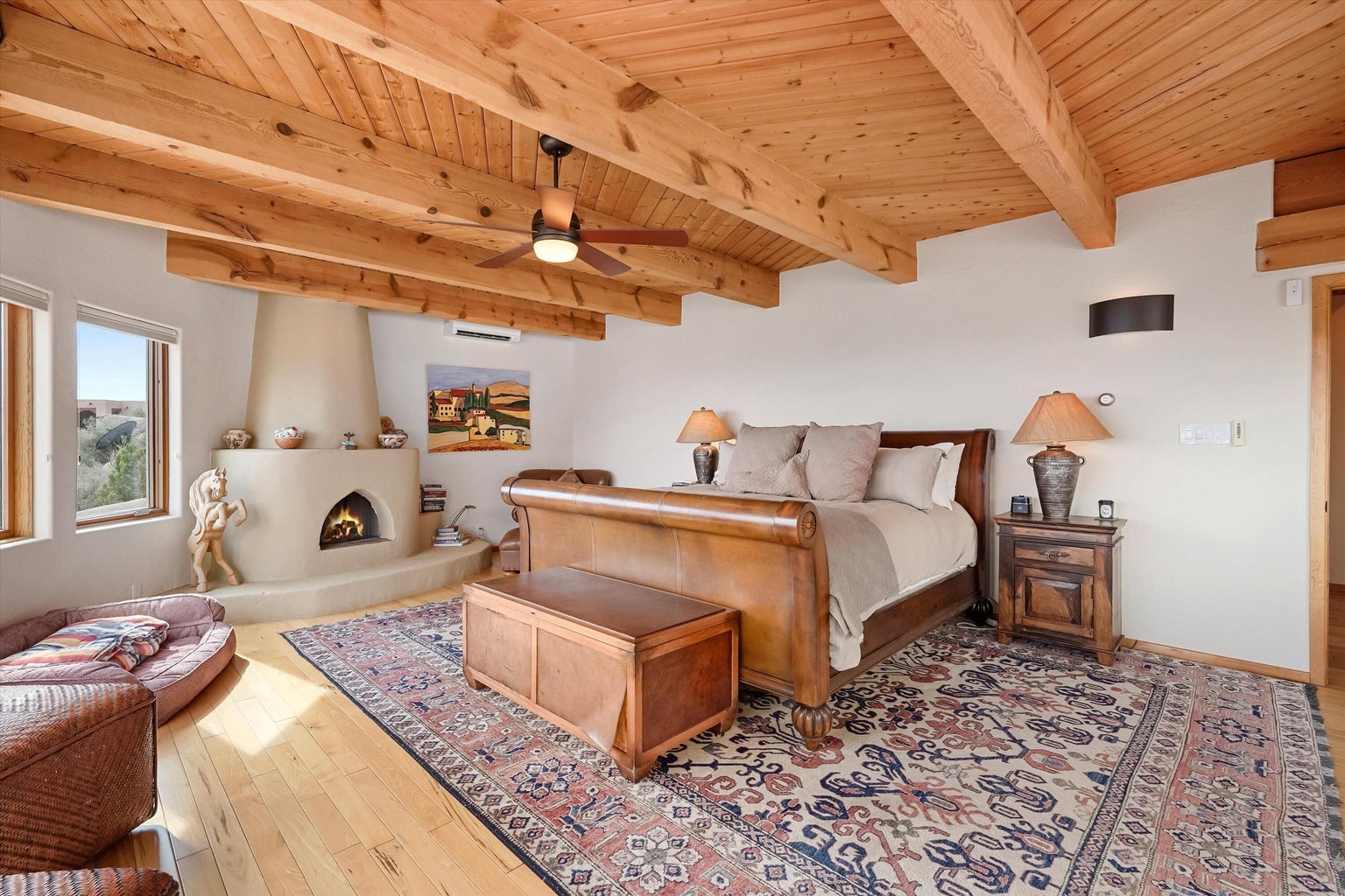 Primary bedroom with wood-beamed ceiling, kiva fireplace, and broad view windows