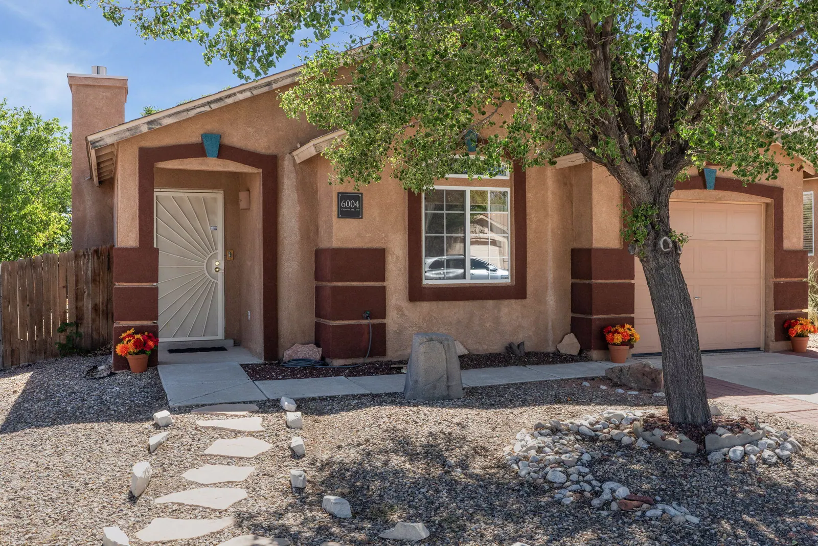 Front exterior of 6004 Cyonus Avenue NW with stucco facade, attached garage, xeriscape, and a mature tree