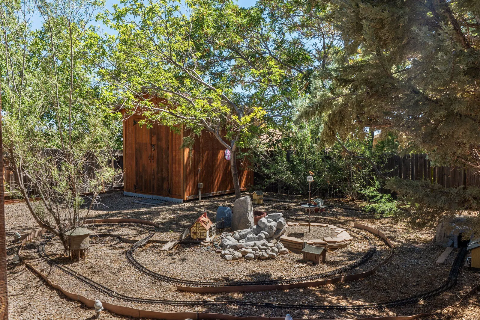 Garden railway track curving through a miniature town beside a stone waterfall feature in the backyard of 6004 Cyonus Avenue NW