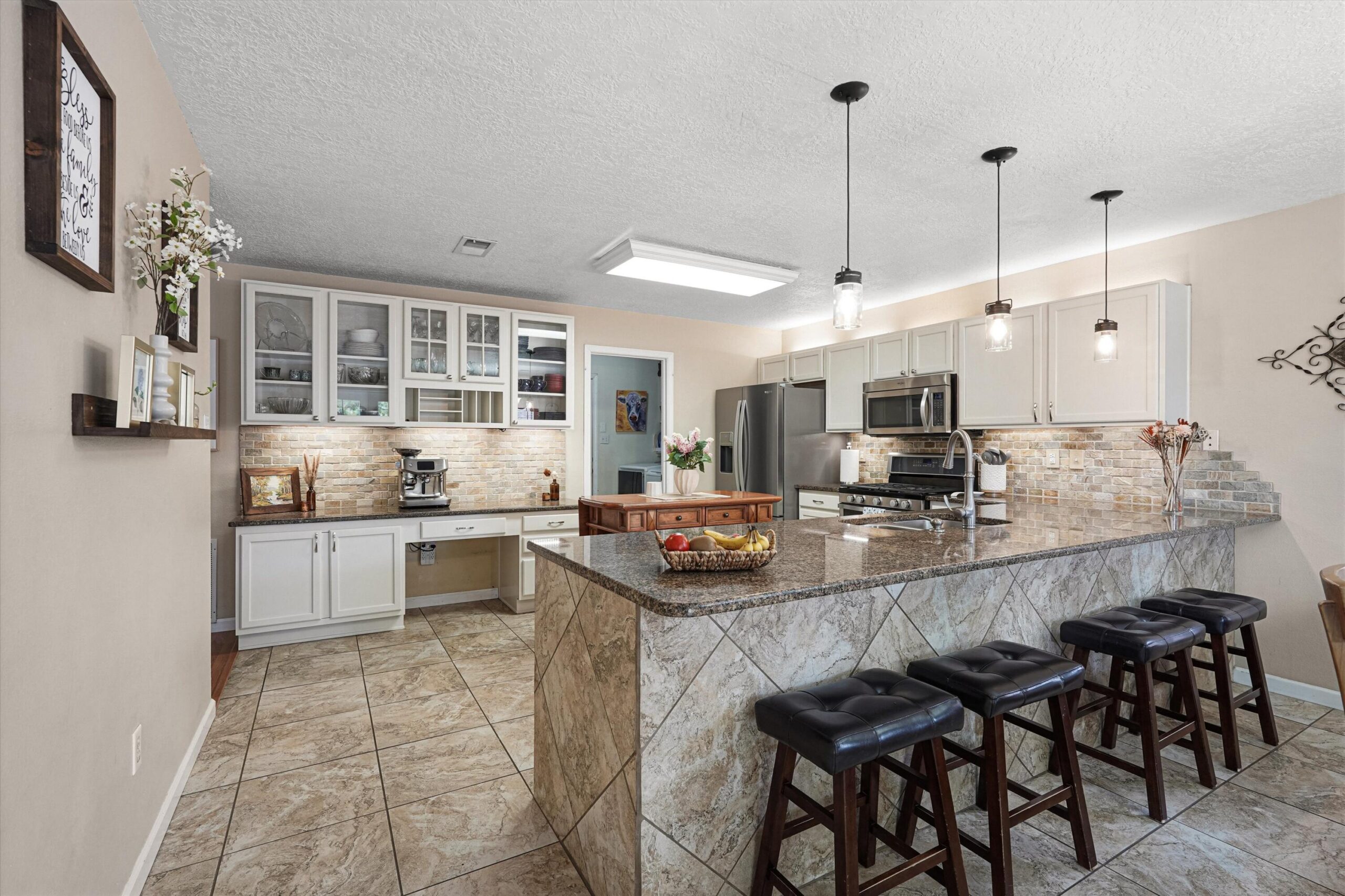 Kitchen with granite peninsula, bar seating, white cabinetry, and stainless appliances