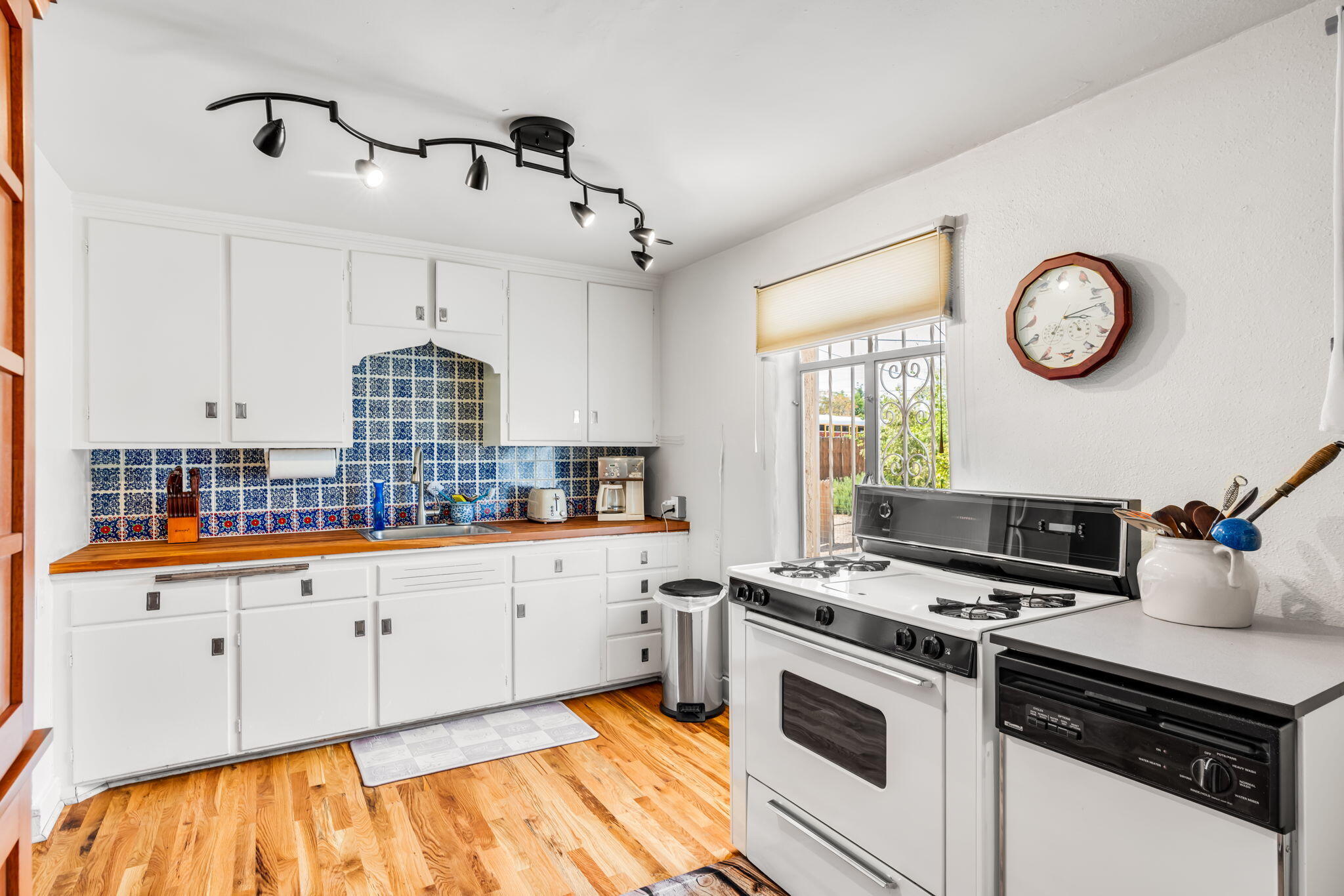 Kitchen at 406 Atrisco Drive SW with white cabinets, wood countertops, blue tile backsplash, gas range, and hardwood flooring