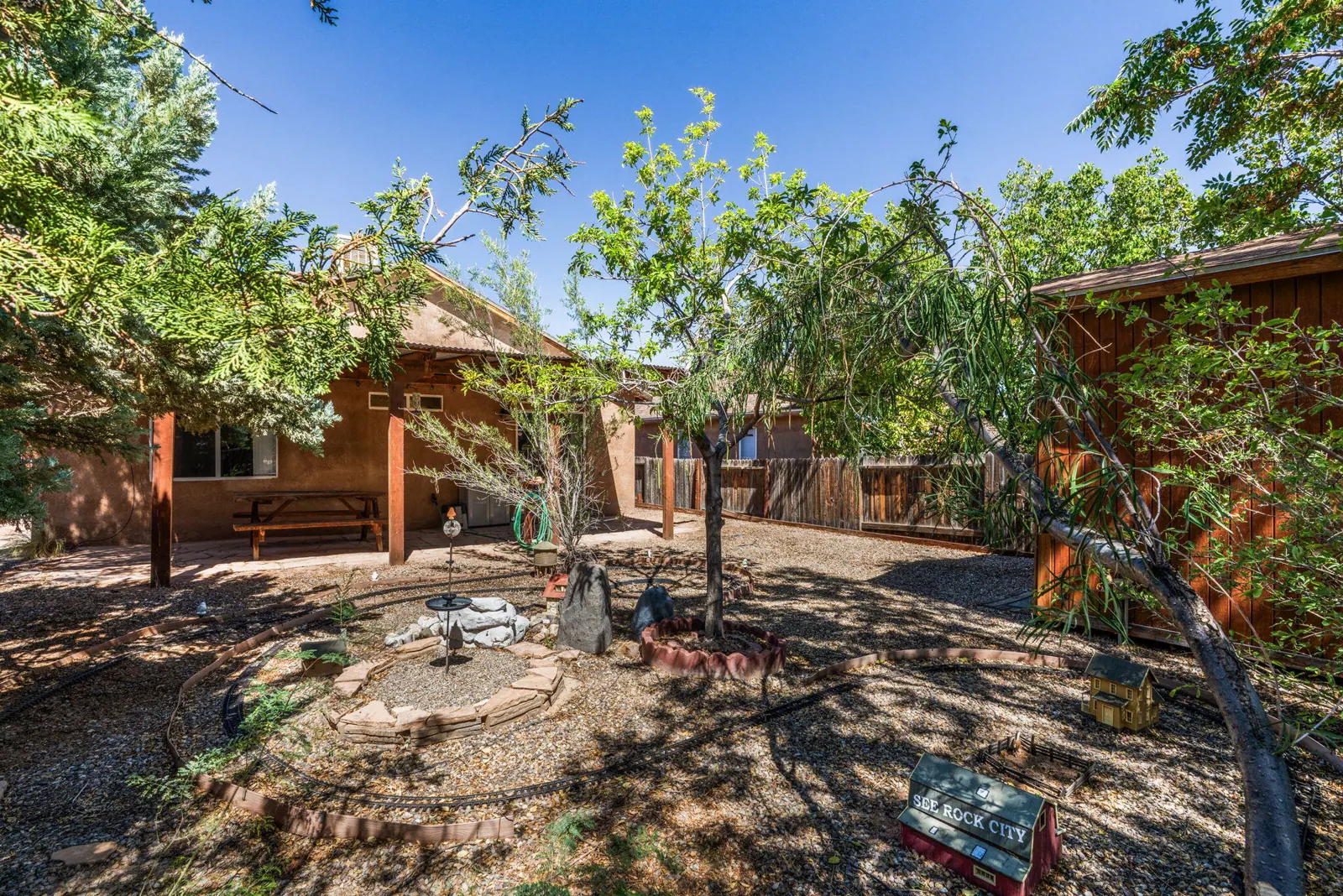 Wide backyard view at 6004 Cyonus Avenue NW with garden railway tracks, mature landscaping, and a covered patio