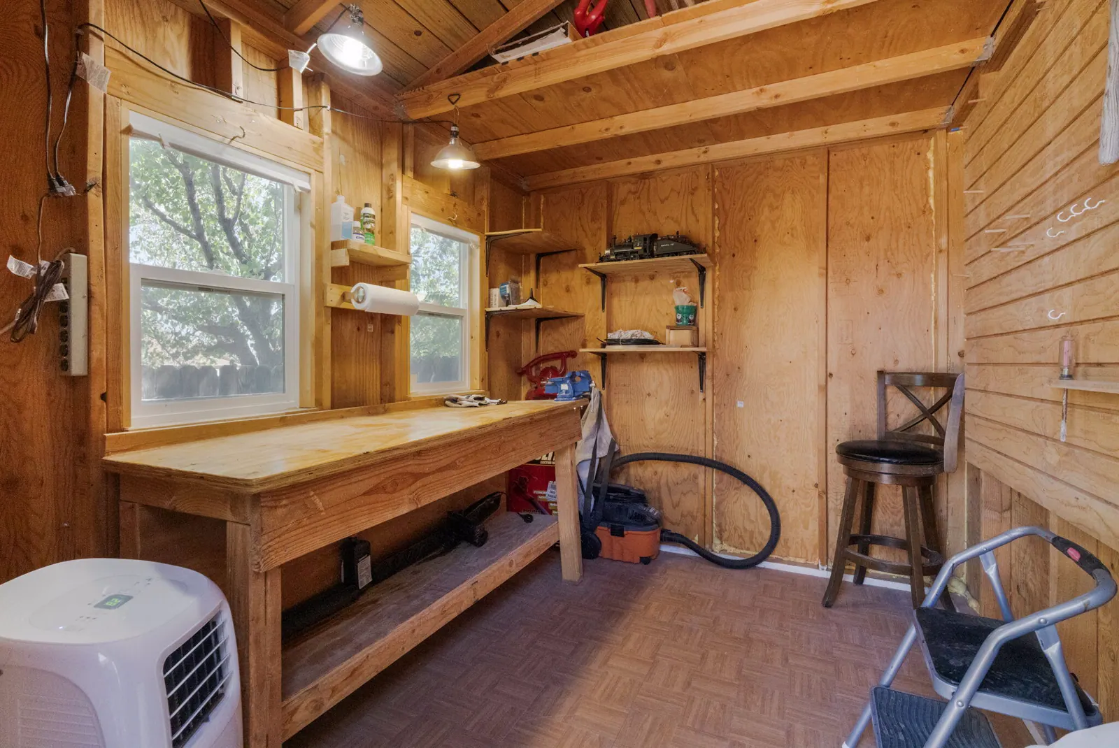 Wood-lined storage shed interior at 6004 Cyonus Avenue NW with a workbench, windows, wall storage, and overhead lights